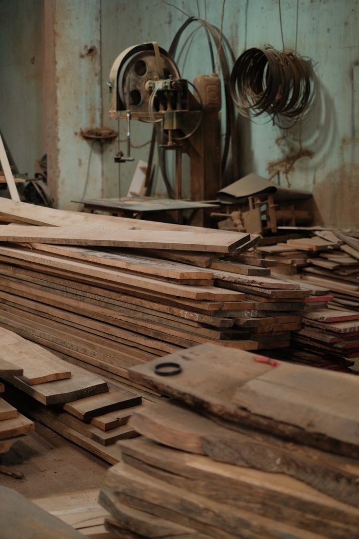 A cluttered workshop filled with stacked wood planks and vintage machinery in a rustic setting.
